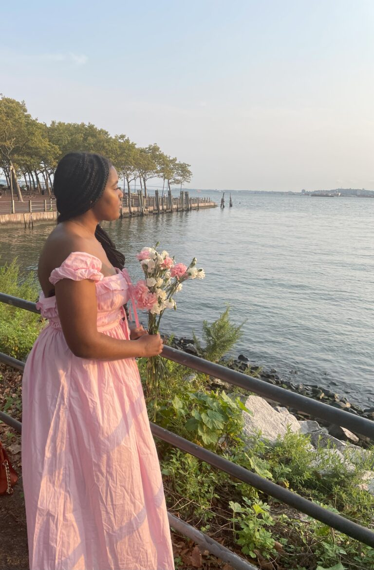 girl stanning next to the shore with a long pink dress on hold bouquet of flowers