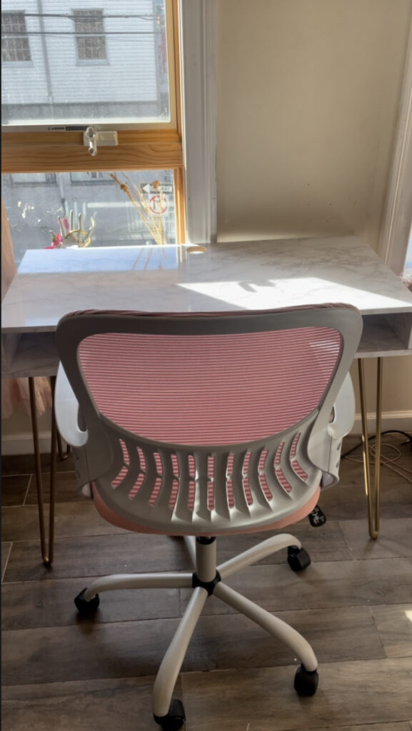 marble desk with pink swivel chair in front of a window